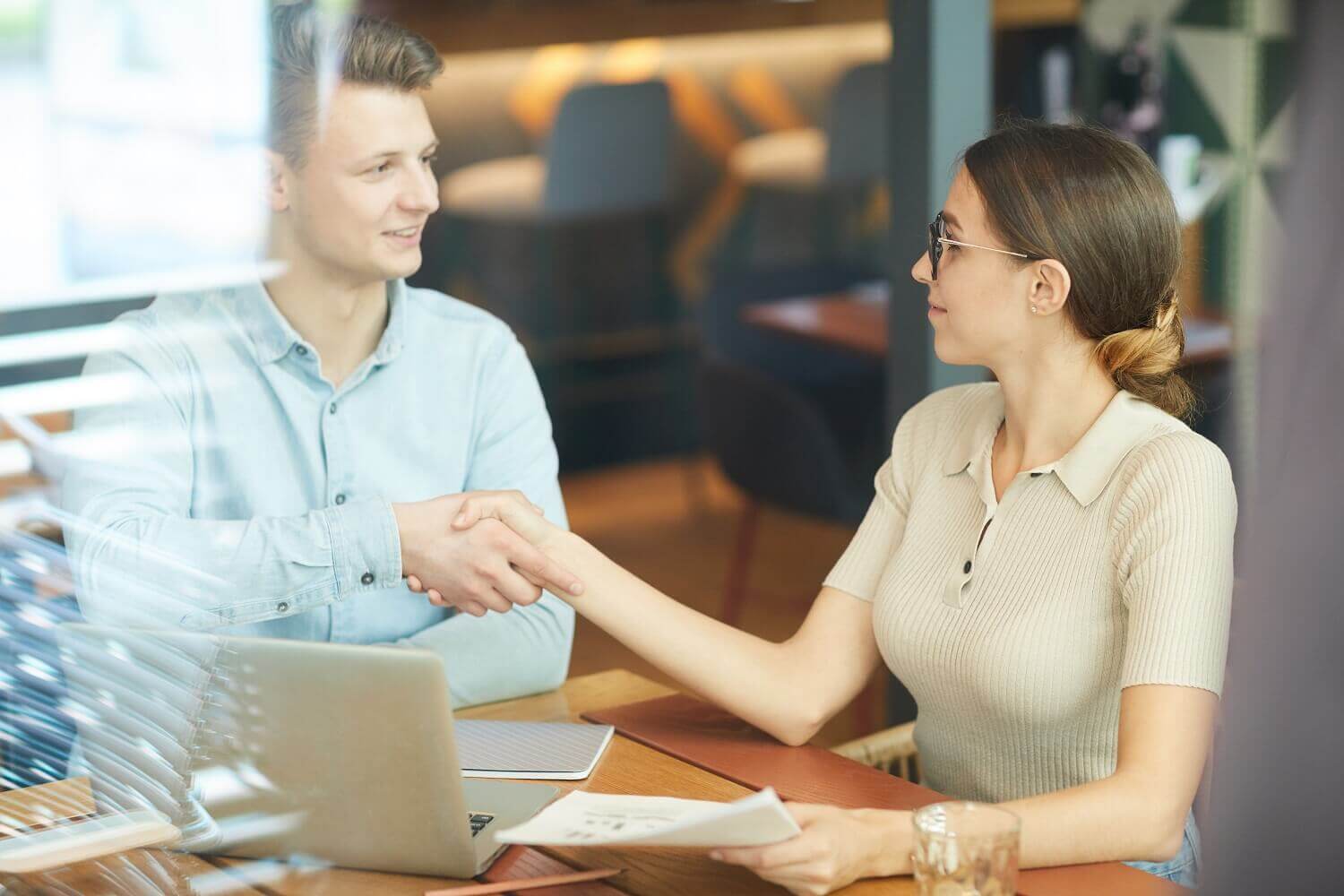 Cliente e dono de agência de marketing digital dando um aperto de mãos após o fechamento de um contrato de serviço bem-sucedido.